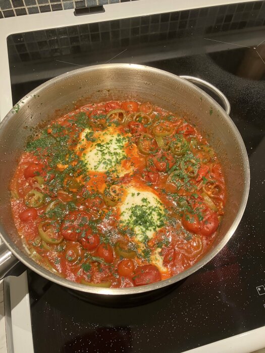 Stekpanna på spis med shakshuka, ägg, tomatsås, paprika och persilja.