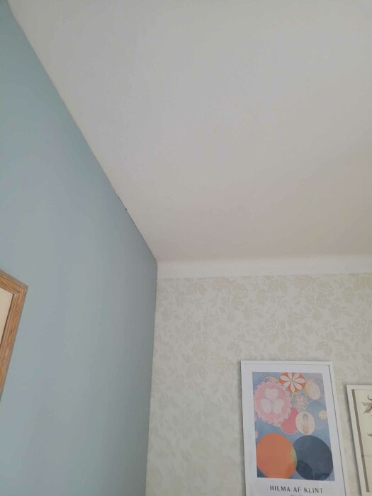 Ett hörn av ett rum med tapet, Hilma af Klint-konst, blå vägg och vit tak.