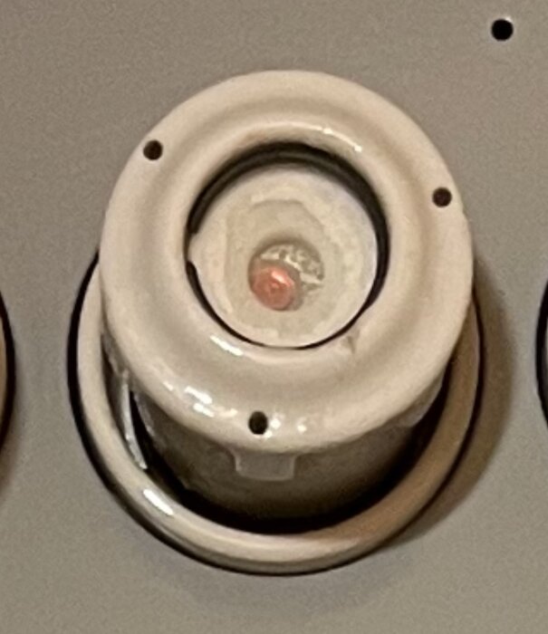 Keramisk isolator med trådar, förmodligen för elektrisk installation, monterad på grå vägg.