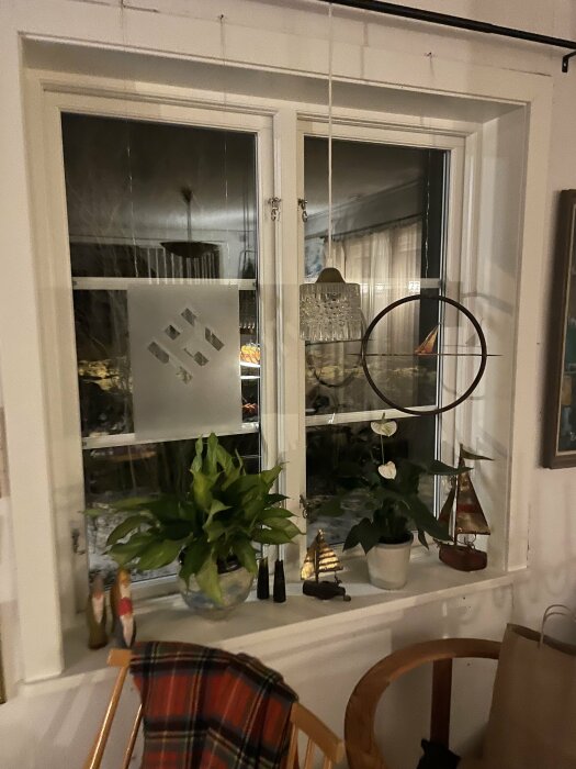 Ett mysigt fönster med växter, dekorativa föremål, och reflektion av inredning. Hygglig atmosfär på kvällen.