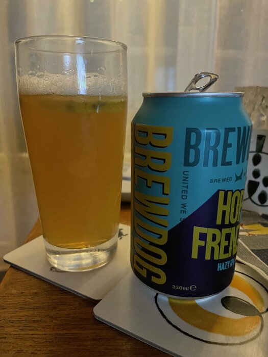 Ölglas med hazy IPA bredvid en BrewDog burk på en underlägg. Inomhus, möjligen i ett hem.