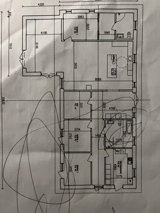 Arkitektonisk ritning av en byggnadsplan med dimensioner och rum uppställda, fotograferad med krångliga linjer ovanpå.