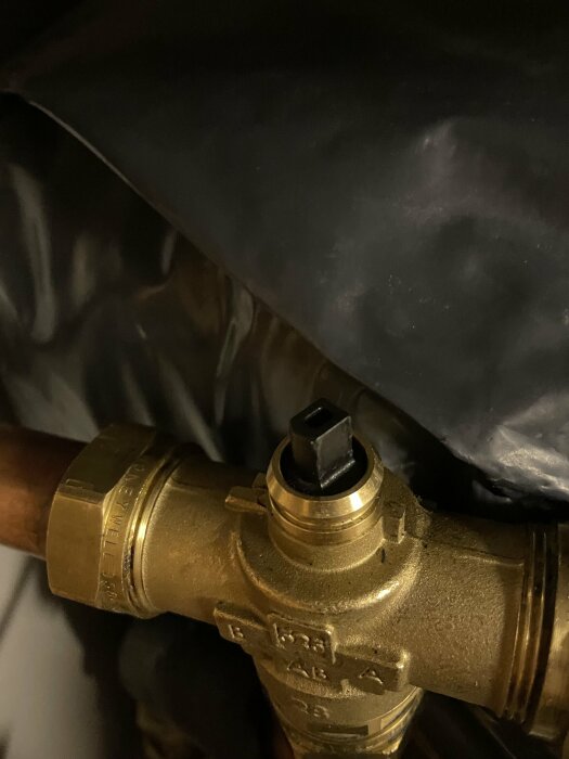 Mässingsventil på rör, svart plastspak, mot dunkel bakgrund. Industriell, teknisk, närbild.