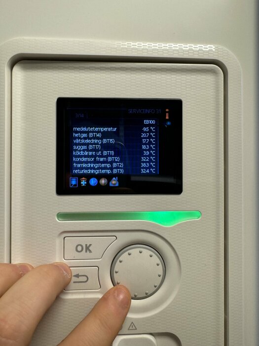 Skärm med temperaturdata, knappar, grönt lysande indikator, någons hand trycker på OK-knapp.