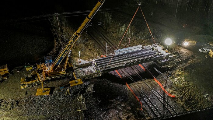 Nattarbete med installation av en ny järnvägsbro med hjälp av mobilkranar och projektionsbelysning.