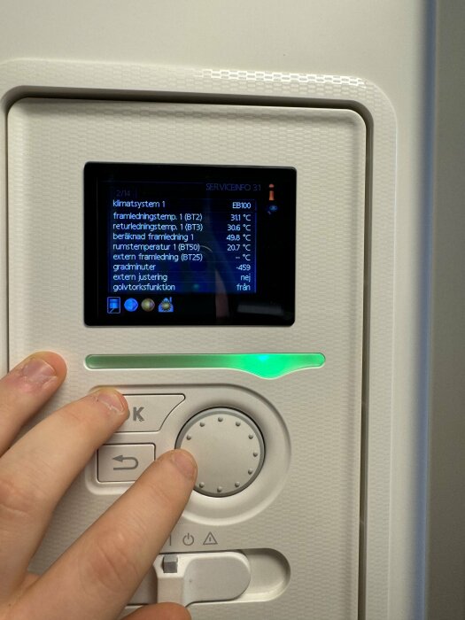 Hand justerar reglage på panel med skärm som visar temperaturinformation för klimatsystem. Grov textur; grön lysdiod indikerar aktivitet.