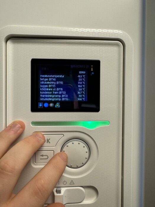 En hand använder en kontrollpanel med skärm som visar temperaturinformation för olika systemkomponenter.
