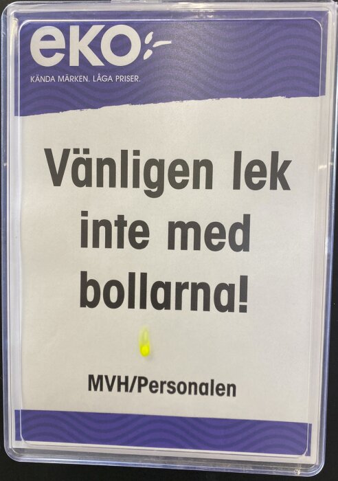 Skylt med text "Vänligen lek inte med bollarna! MVH/Personalen", Eko-logotyp, plastficka, gult klistermärke.