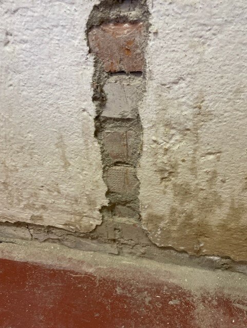 Skadad vägg med flagnande vitmålning avslöjar underliggande röda tegelstenar och murbruk. Behöver renovering eller reparation.