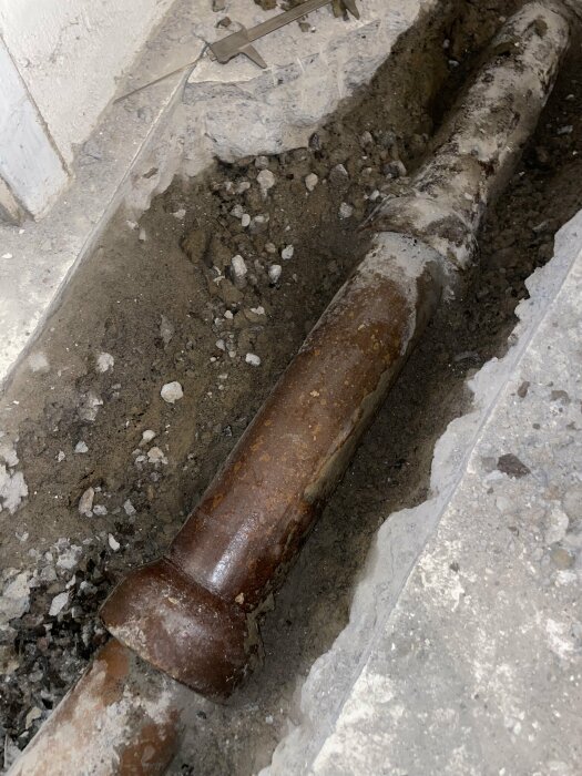En gammal rostig rörledning grävdes fram ur betonggolv med grus och smuts runt omkring.