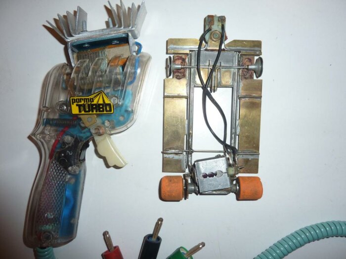 Två genomskinliga plastobjekt: en leksakspistol och en okänd apparat, elektriska komponenter, trådar, metallkontakter.