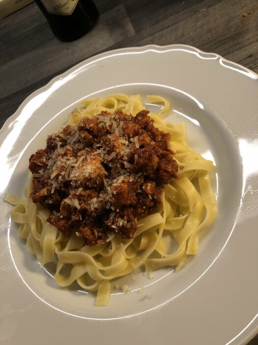 Tallrik med fettuccinepasta toppad med köttsås och parmesan, serverad på ett vitt fat.