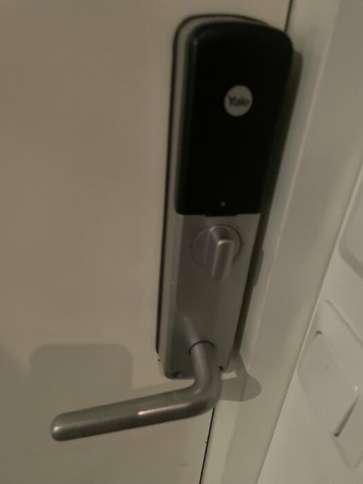 Dörrhandtag med elektroniskt lås och Yale-varumärke på en vit dörr. Suddig och mörk bild.