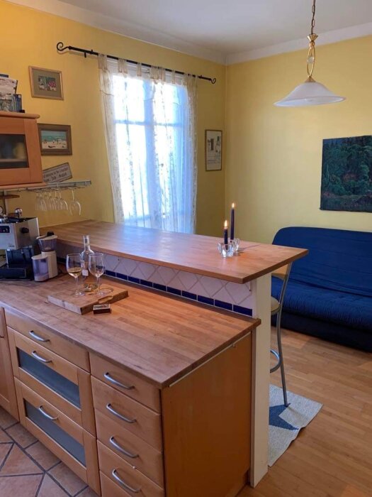 Ett mysigt kök med gult vägg, trämöbler, blå soffa, tända ljus och en vit gardin.