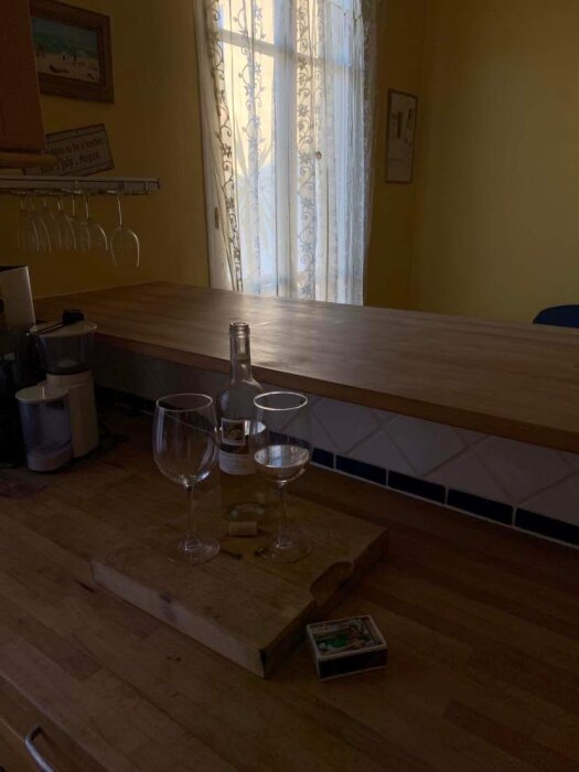 Ett kök med bordsyta, tom flaska, två vinglas och tändstickor på en träskärbräda.