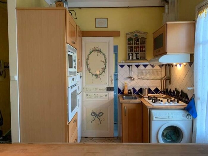 Ett mysigt kök med träskåp, vitvaror, kakel, kylskåp, och en dekorativ krans på dörren.