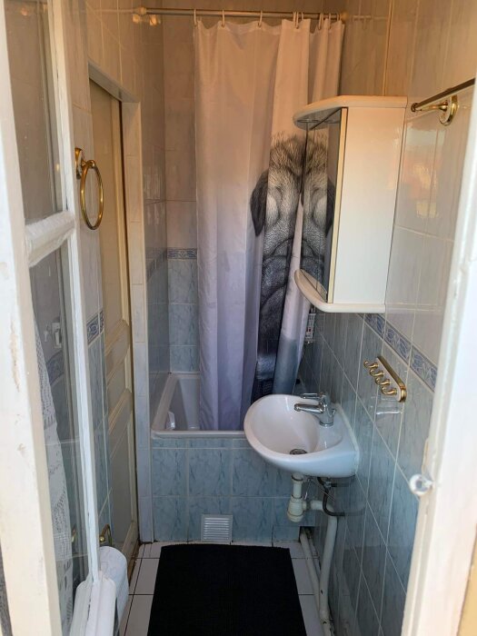 Ett litet badrum med duschdraperi, handfat, spegelskåp och blå kakelväggar.