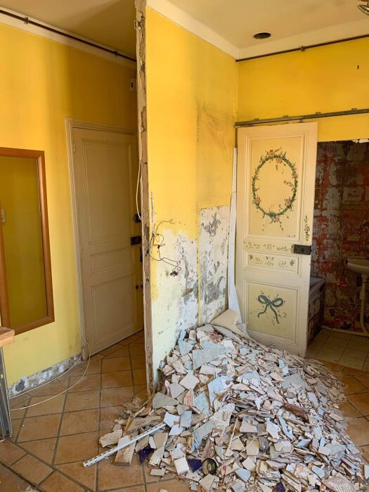 Rum under renovering, nedrivna väggar, rörigt, hög med rivningsavfall, gammal kakel på golvet.