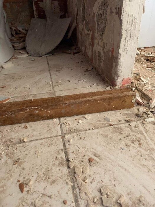 En nedsmutsad plats med spillror, trälist, skottkärra vid en nedsliten vägg. Renovering eller rivning pågår.