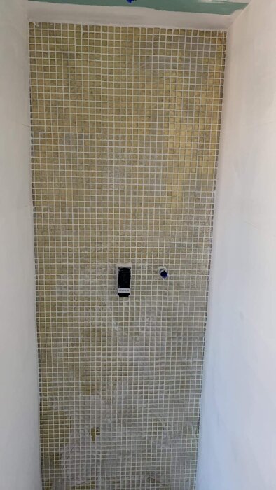 Kaklad vägg i dusch med öppning för blandare och duschhuvud, ofullständig renovering.
