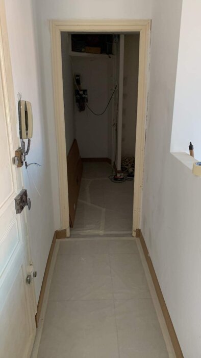En korridor i ett hem under renovering, skyddspapp på golvet, dörröppning framåt, oavslutade elektriska installationer.