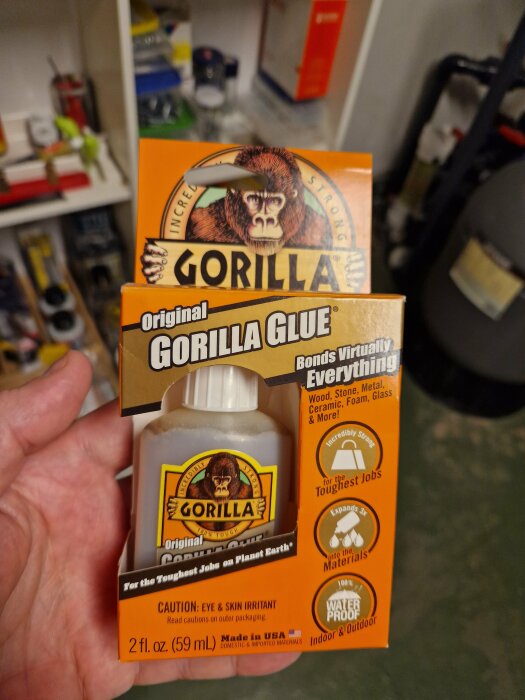 Gorilla Glue, starkt lim i förpackning, hålls upp, bakgrund suddig, limflaska synlig, varnings- och produktinformation.