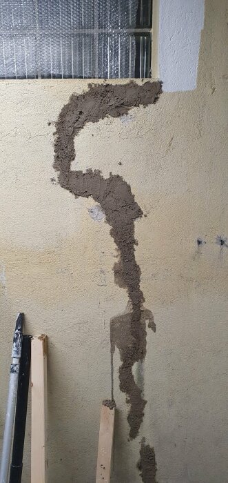 Reparation av vägg pågår, putsbruk applicerat ojämnt, verktyg och brädor synliga.