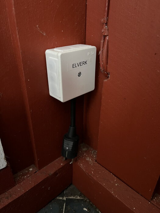 Eluttag märkt "ELVERK" på röd vägg, med ansluten kontakt och synlig kabel.