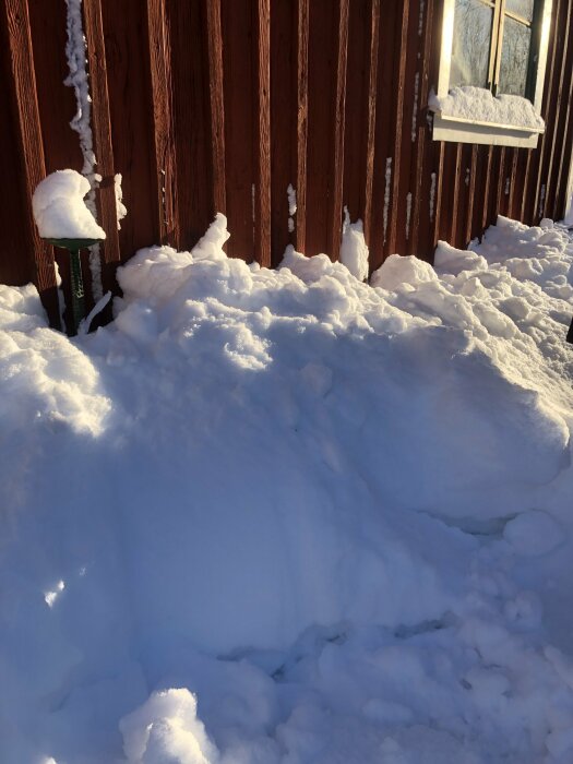 Snö täcker trädgårdsredskap vid trästaket, solig dag, vinterscen, snödrivor, reflektion av solljus.