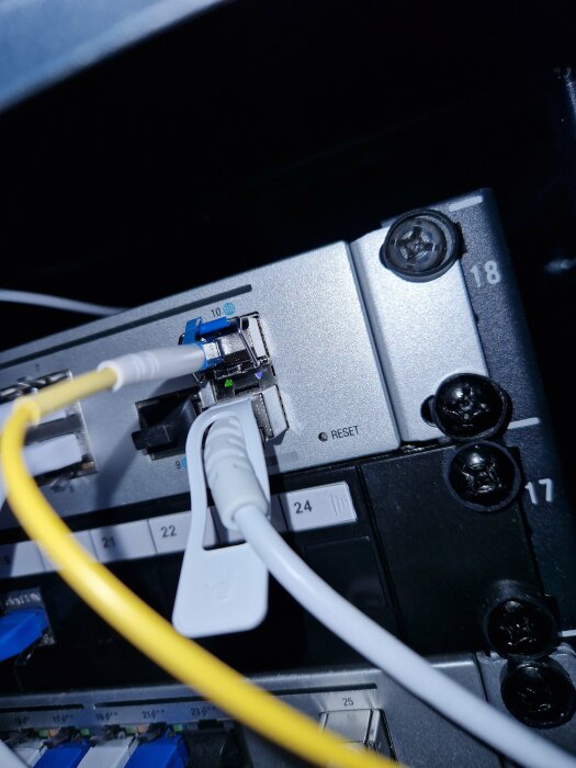 Nätverksutrustning med Ethernet-kablar anslutna till switch-portar, numrerade, reset-knapp synlig.