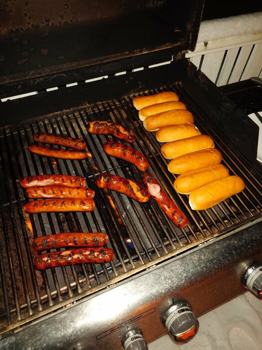 Grillade korvar och bröd på en gasolgrill utomhus, kvällsljus, matlagning, grillfest-stämning.