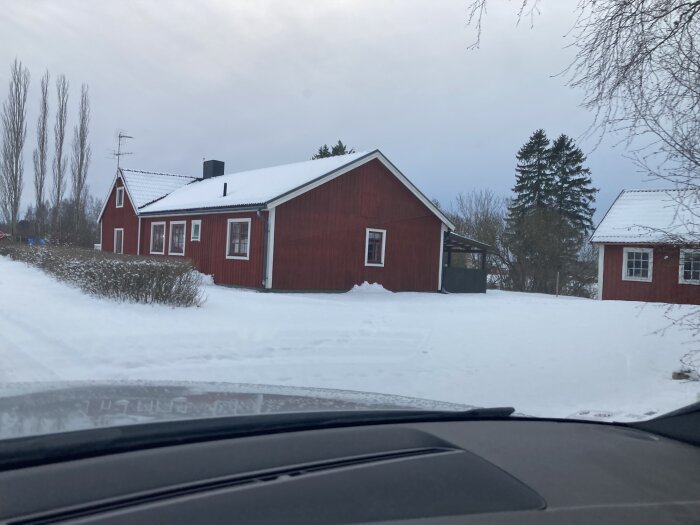 Röda trähus, snötäckt landskap, vinter, molnigt, bilutsikt, lugnt bostadsområde, trädbakgrund, traditionell svensk byggnadsstil.