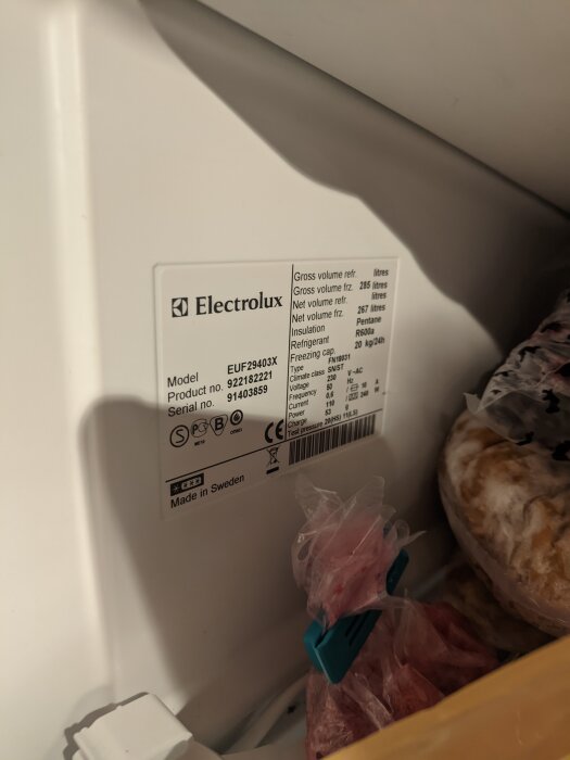 Etikett på kylskåp från Electrolux med modellinformation och specifikationer, omgiven av matvaror i plastpåsar.