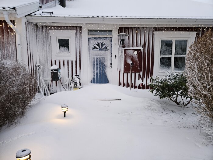 Ett snöigt hus med istappar, belyst gångväg, tidig kväll, vinterdekorationer, hemtrevlig atmosfär.