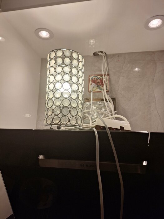 Dekorativ lampa på diskmaskin, röriga kablar, marmorbakgrund, infällda taklampor, köksmiljö.