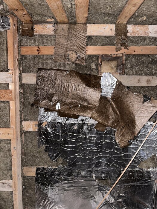 Bild av skadad isolering och träkonstruktion i tak, med synliga skador och urfallande isoleringsmaterial.