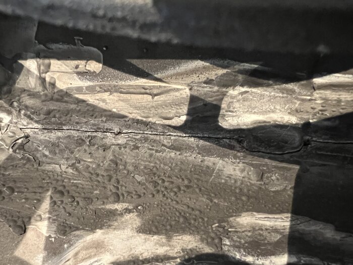 Textur av vått trä och murbruk i svartvitt, med vattendroppar och skuggor, närbild.