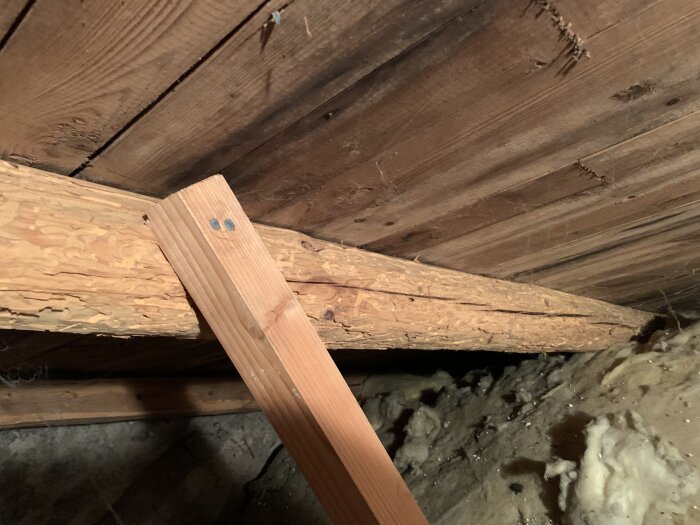 Trästödbjälke installerad intill skadad takbjälke i ett mörkt vindutrymme.