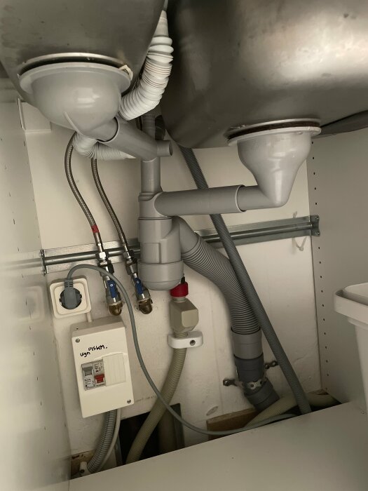 Undersidan av en handfat med rörkopplingar, vattenledningar, och installationsboxar för vatten och elektricitet.