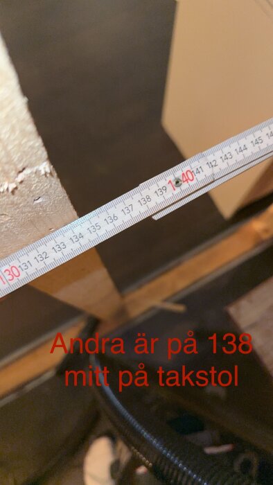 Måttband visar 138 centimeter på trämöbel, text markerar mätningen, suddig bakgrund.