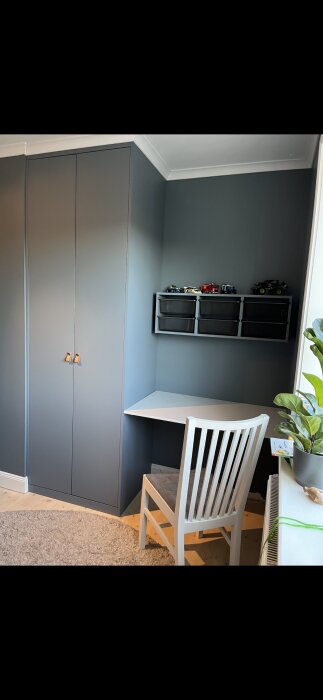 Ett arbetsrum med garderober, skrivbord, stol, hyllor och leksaksbilar. Neutralt färgschema. Modernt och minimalistiskt.