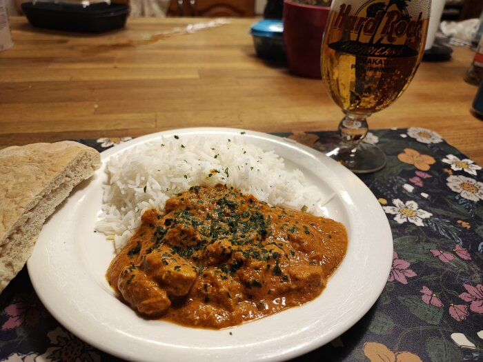 Indisk curry med ris, bröd och öl i Hard Rock Cafe-glas på blommigt bord.