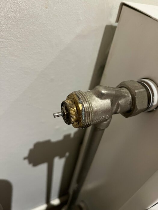 Termostatventil för radiator, närbild, vägg i bakgrunden, skugga, ingen radiatorhuvud, inomhus.