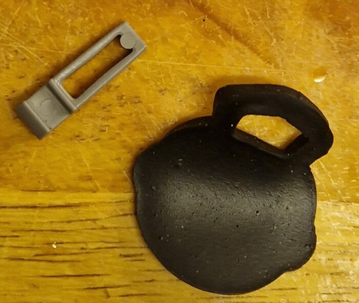 Ett svart kettlebell-liknande föremål och en grå plastdel på träbakgrund.