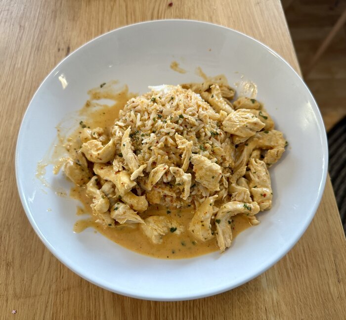 Krämig pasta med kyckling och parmesan, toppad med örter, på träbord.