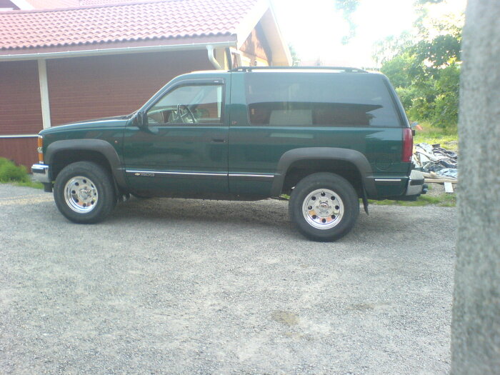 Grön pickup truck parkerad utomhus nära byggnad och grusväg.