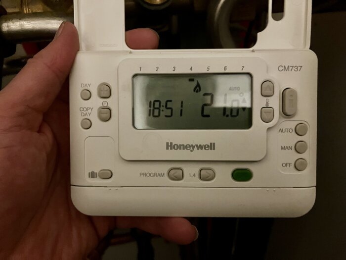 En hand som håller en Honeywell termostat med tid och temperaturdisplay.