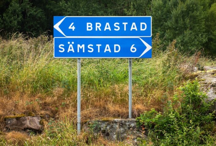 Svensk vägskylt visar avstånd till Brastad åt vänster och Sämstad åt höger mot naturbakgrund.