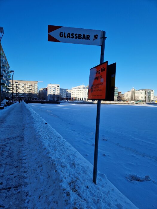 Vinterstadsscen vid fruset vatten, skylt för glassbar, klarblå himmel, inga personer synliga.