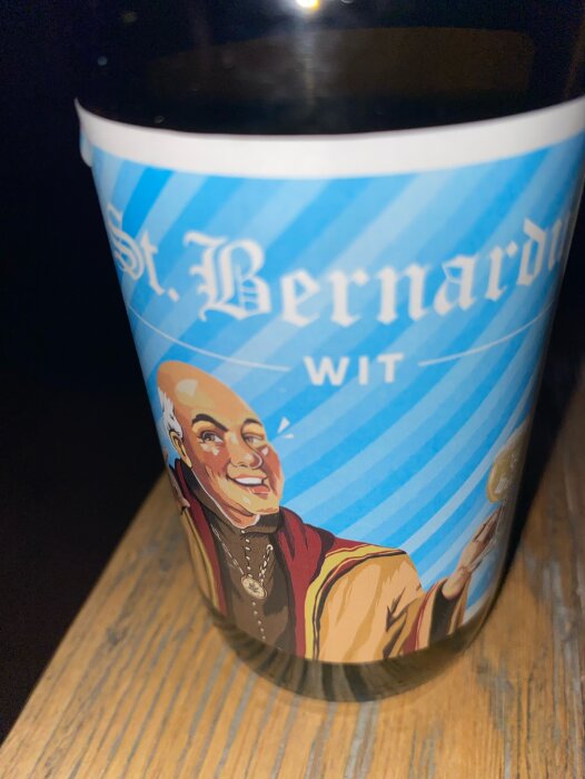 Ölflaska med etikett som föreställer tecknad munk, "St. Bernardus Wit", på träyta.